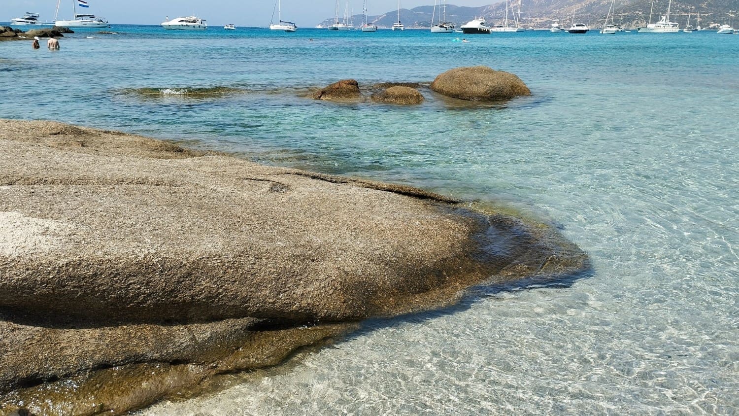 Scoglio e mare cristallino con barche all'orizzonte